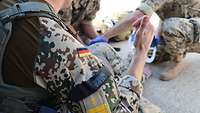 Mehrere Soldaten hocken um einen weiteren Soldaten und behandeln ihn. 