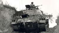 Auf einem Schwarz-Weiß-Foto steht ein Panzer auf einem Sandweg neben einem Erdwall.