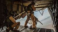 Im Heck eines fliegenden Hubschraubers steht ein Soldat am Maschinengewehr.
