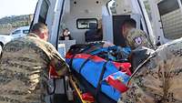 Der Verletzte wird auf einer Trage von mehreren Soldaten in den Krankenwagen geschoben.