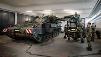 In einer Halle stehen mehrere Soldaten um eine Haubitze herum.