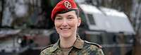 Eine Soldatin blickt freundlich in die Kamera. Im Hintergrund steht eine Panzerhaubitze.