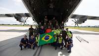 Mehrere Personen vor der Laderampe eines Transportflugzeugs zeigen eine brasilianische Flagge.