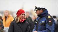 Ein Marinesoldat in blauer Uniform im Gespräch mit einer Frau im schwarzem Wintermantel