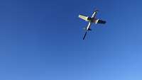 Ein Propellerflugzeug zieht am blauen Himmel einen Schleppsack hinter sich her.