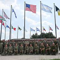 Viele Soldaten aus verschiedenen Ländern stehen vor Flaggenmasten.