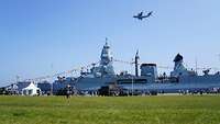 Über einem Schiff der deutschen Kriegsmarine fliegt ein Transportflugzeug der Luftwaffe.
