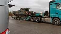 Ein Schützenpanzer steht mit Ketten verzurrt auf einem blauen Lastwagen.