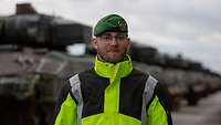 Ein Soldat in signalgrüner Jacke steht vor einer Kolonne vieler Panzer