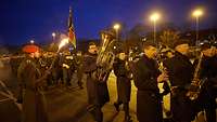 Mehrere Soldaten marschieren in Dunkelheit, an vordester Front ist das Musikkorps.