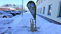 Ein Schlitten vor der Beachflag, die im Schnee steht.
