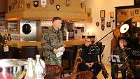 Ein Soldat steht in einem Raum und spricht zu den Anwesenden.