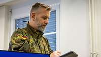 Ein Soldat steht mit einem Klemmbrett in einem Raum zwischen Monitoren.