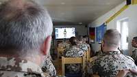 Mehrere Soldaten sitzen in einem Raum. Hinten sieht man eine Leinwand, mit deren Hilfe der Unterricht gehalten wird.