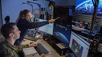 Eine Soldatin zeigt einem Soldaten, der an seinem Arbeitsplatz sitzt, etwas auf einem Monitor