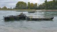 Zwei Motorboote schieben zwei Faltschwimmbrücken im Wasser vor sich, um diese zusammenzuführen