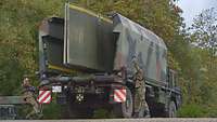 Zwei Soldaten ziehen links und rechts an einem Hebel an einem Fahrzeug mit einer Faltschwimmbrücke