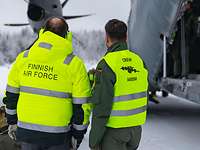 Ankunft bei der finnischen Luftwaffe Zwei Männer in gelber Weste stehen auf Landebahn in Winter neben Ladeluke eines Militärflugzeuges