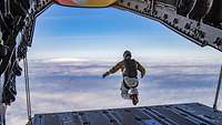 Ein Soldat mit Fallschirmrucksack springt hinten aus einem Flugzeug in Wolken unter blauem Himmel