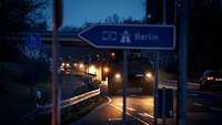 Schwere Fahrzeuge rollen im Dunkeln im Konvoi über die Autobahn. Ihre Scheinwerfer leuchten auf.
