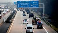 Ein Militärkonvoi passiert ein Autobahnkreuz. Über der Straße sind blaue Hinweisschilder angebracht.