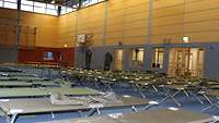 Mehrere Reihen Feldbetten in einer Turnhalle 