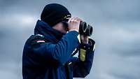 Ein Soldat in Uniform steht mit einem Fernglas zugeschneit auf der Nock