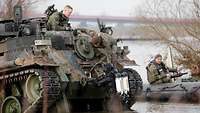 Ein Taucher und ein Panzer stehen nah am Ufer im Wasser.
