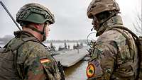 Ein deutscher und ein britischer Soldat stehen am Ufer und sprechen miteinander.