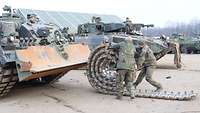 Soldaten rollen die Kette eines Schützenpanzers auf.