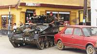 Soldaten fahren mit einem Kettenfahrzeug über die Straßen Prizrens an einem roten Auto vorbei