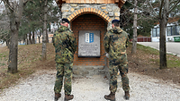Zwei Soldaten stehen vor einem Gedenkstein, der von Bäumen umringt ist