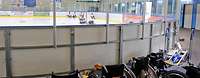 Rollstühle vor der Bande eines Eishockeyfeldes. Wehrdienstbeschädigte spielen Eishockey.