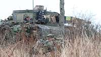 Ein abgesessener Soldat mit Waffe im Anschlag, daneben ein Schützenpanzer