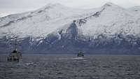 Zwei Kriegsschiffe auf dem Meer vor einem schneebedeckten Bergen.