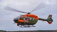Ein Hubschrauber mit orangefarbener Lackierung schwebt knapp über dem Boden