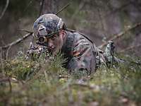Gefechtsbereit Ein Soldat liegt im Wald hinter einem Baum mit der Waffe im Anschlag.