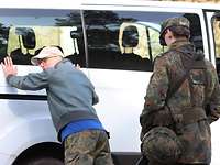 Checkpoint: verschärfte Personenkontrolle Ein Mann mit grauer Jacke lehnt sich mit den Händen an einen weißen Van. Neben ihm steht ein Soldat.