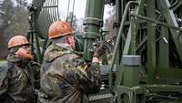 Zwei Soldaten bauen einen großen Antennenmast ab. 