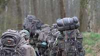 Soldatinnen und Soldaten marschieren schwer bepackt durch den Wald