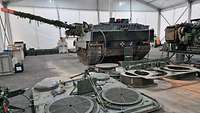 In einem großen, weißen Zelt steht ein Panzer. Davor liegen Ersatzteile.