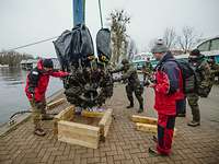Ein Flugzeugmotor wird mit einem Kran sowie Führungsseilen von mehreren Personen aus dem Wasser geborgen