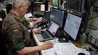 A man wearing a uniform is sitting in front of several screens.
