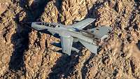 A combat aircraft viewed from above in flight over mountainous terrain