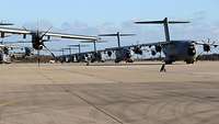 Several transport aircraft are parked at an air base in an orderly row.