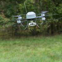 Eine Drohne vom Typ MIKADO im Flug als Portraitaufnahme. ImHintergund steht ein Soldat.