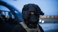 A soldier is wearing a helmet. His face is covered by a piece of cloth; he is looking through binoculars.