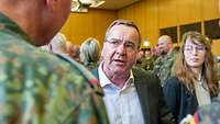 Ein Mann im Anzug steht in einem Raum mit Soldatinnen und Soldaten und spricht mit ihnen