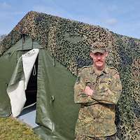Ein Soldat steht mit verschränkten Armen vor einem grünen Zelt