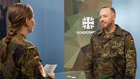 Eine Soldatin interviewt einen Soldaten vor einem Bildschirm in einem Studio